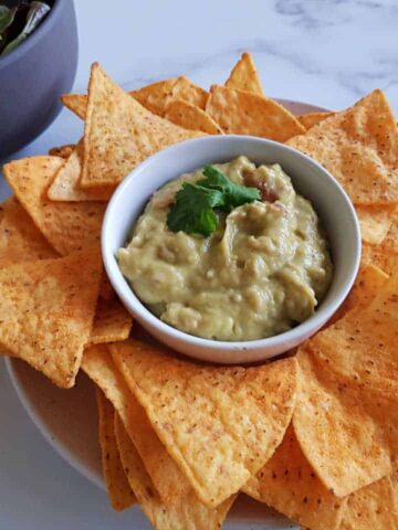 Creamy guacamole on a plate of nachos on a marble table.