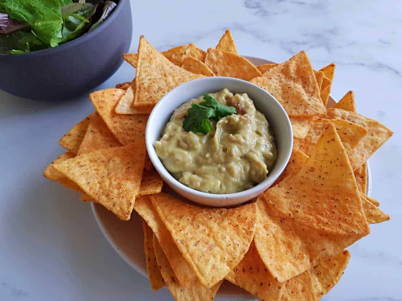 Creamy guacamole on a plate of nachos on a marble table.