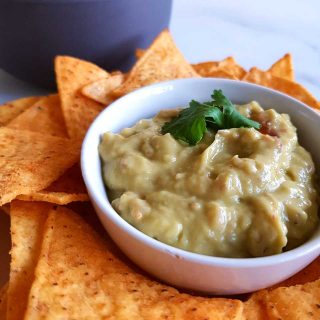 guacamole in a bowl, with tortilla chips on the side.