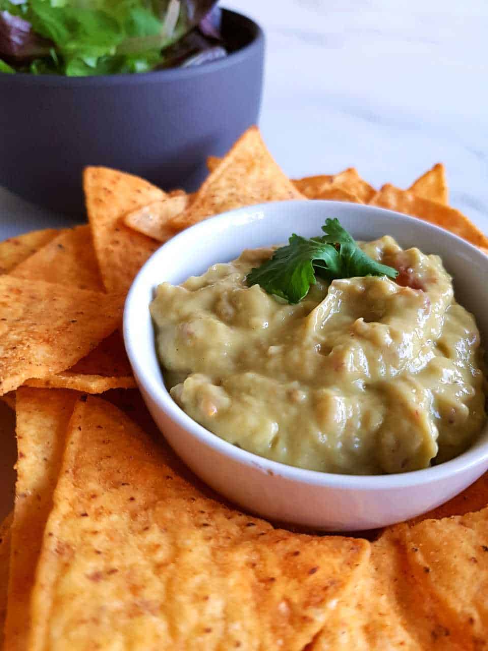 Guacamole with lemon in a white bowl surrounded by nachos.