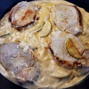 Pork chops with apple cream sauce in a cast iron skillet.