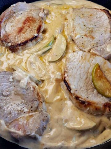 Pork chops with apple cream sauce in a cast iron skillet.