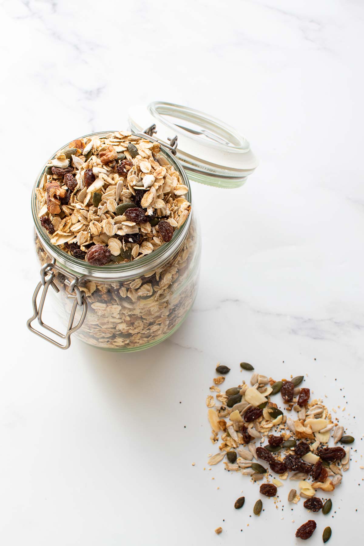 Muesli in a jar, with some muesli scattered around on a marble table.