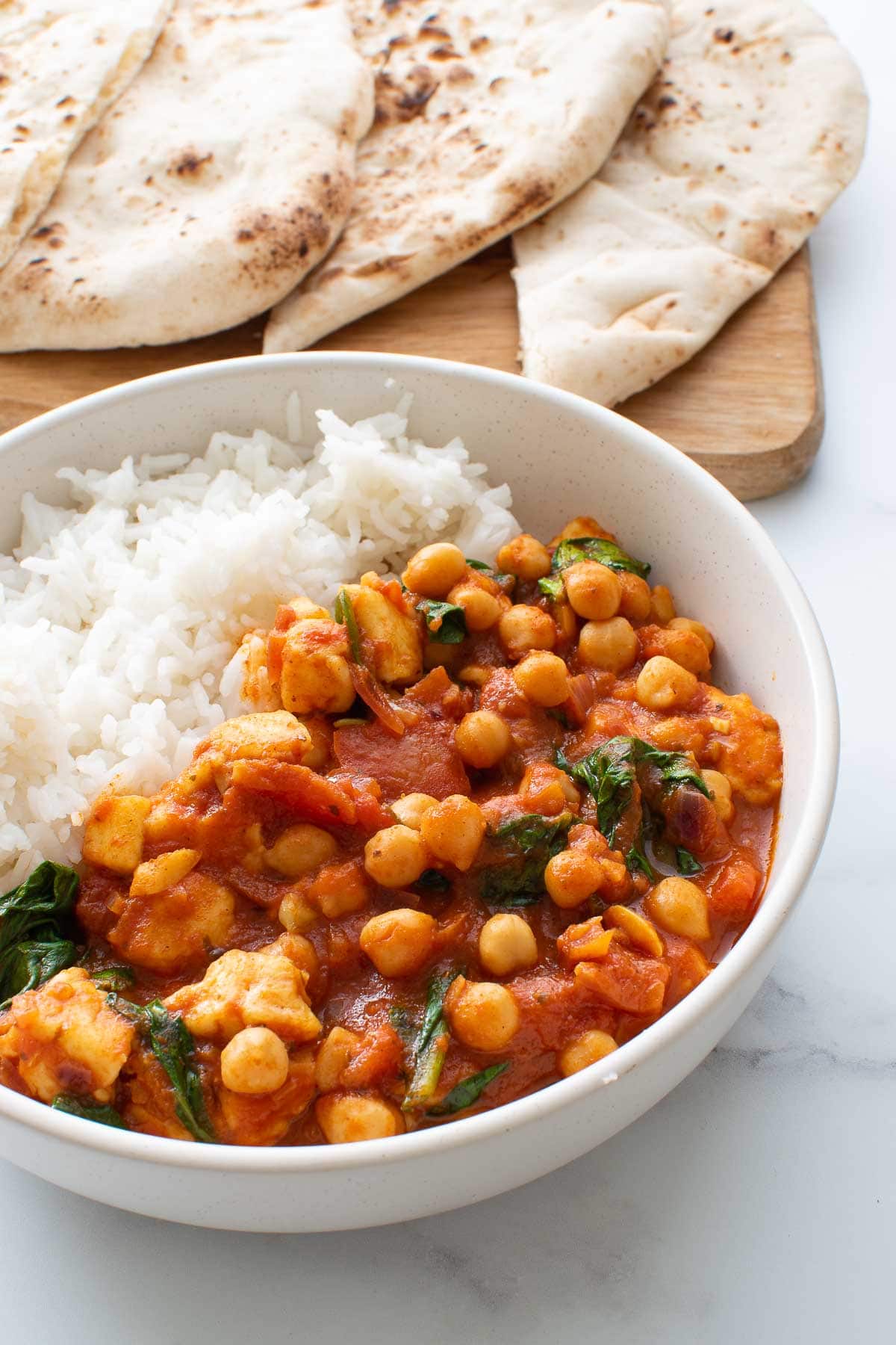 A bowl of chickpea and halloumi curry with rice, and naan in the background.