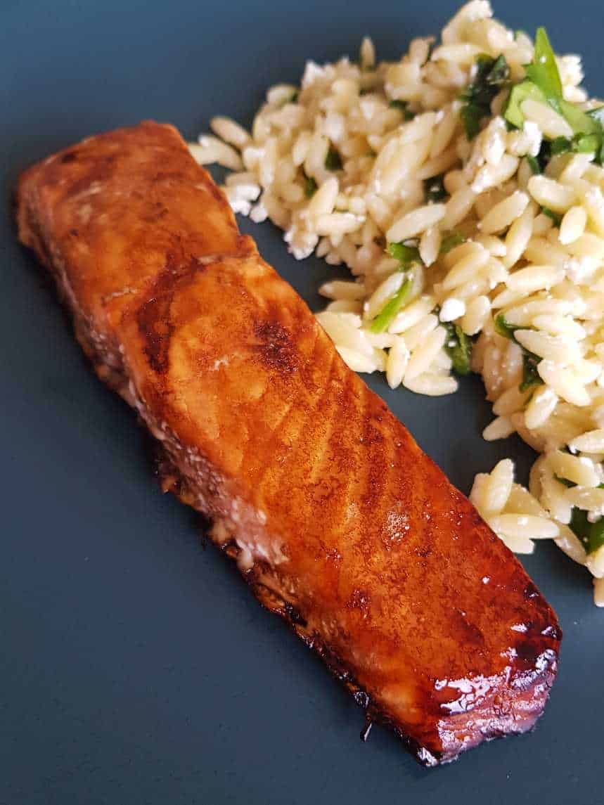 Balsamic and maple glazed salmon on a blue plate with salad in the background.