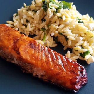 Balsamic maple glazed salmon on a blue plate with salad in the background.