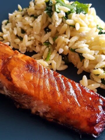 Balsamic maple glazed salmon on a blue plate with salad in the background.