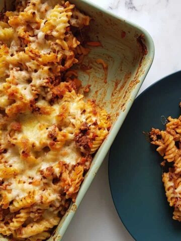 Beef pasta bake in a casserole dish with a plated portion on the side, on a marble table.