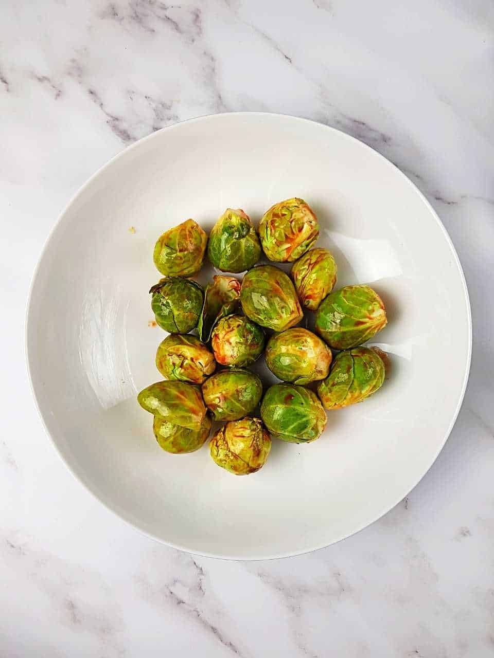 Brussels sprouts with sriracha and honey on a white plate on a marble table.