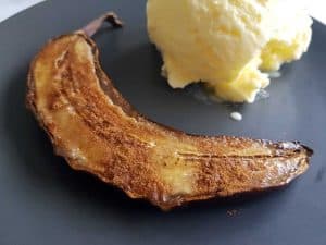 Caramelized oven baked banana on a black plate with ice cream.