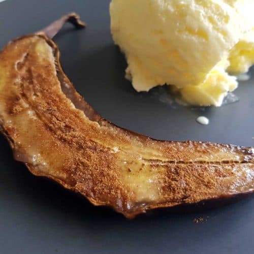Caramelized oven baked banana on a black plate with ice cream.