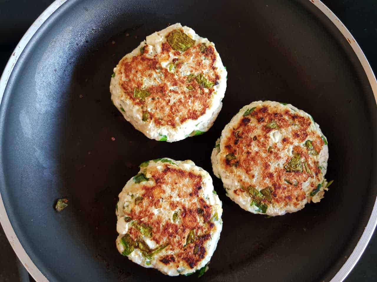 Three cooked turkey burger patties in a frying pan.