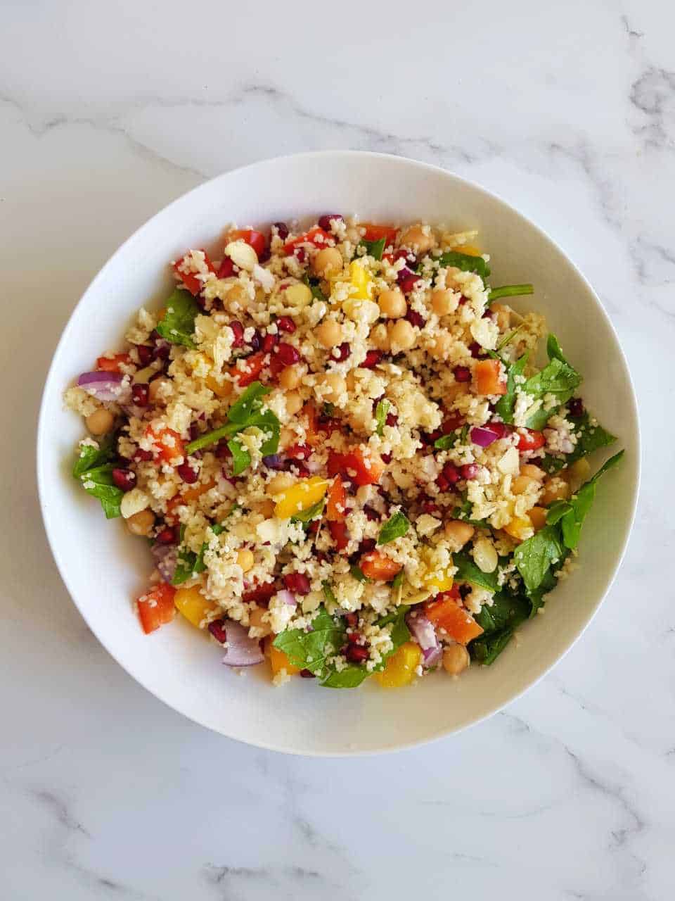 Couscous salad with pomegranate in a white bowl on a marble table