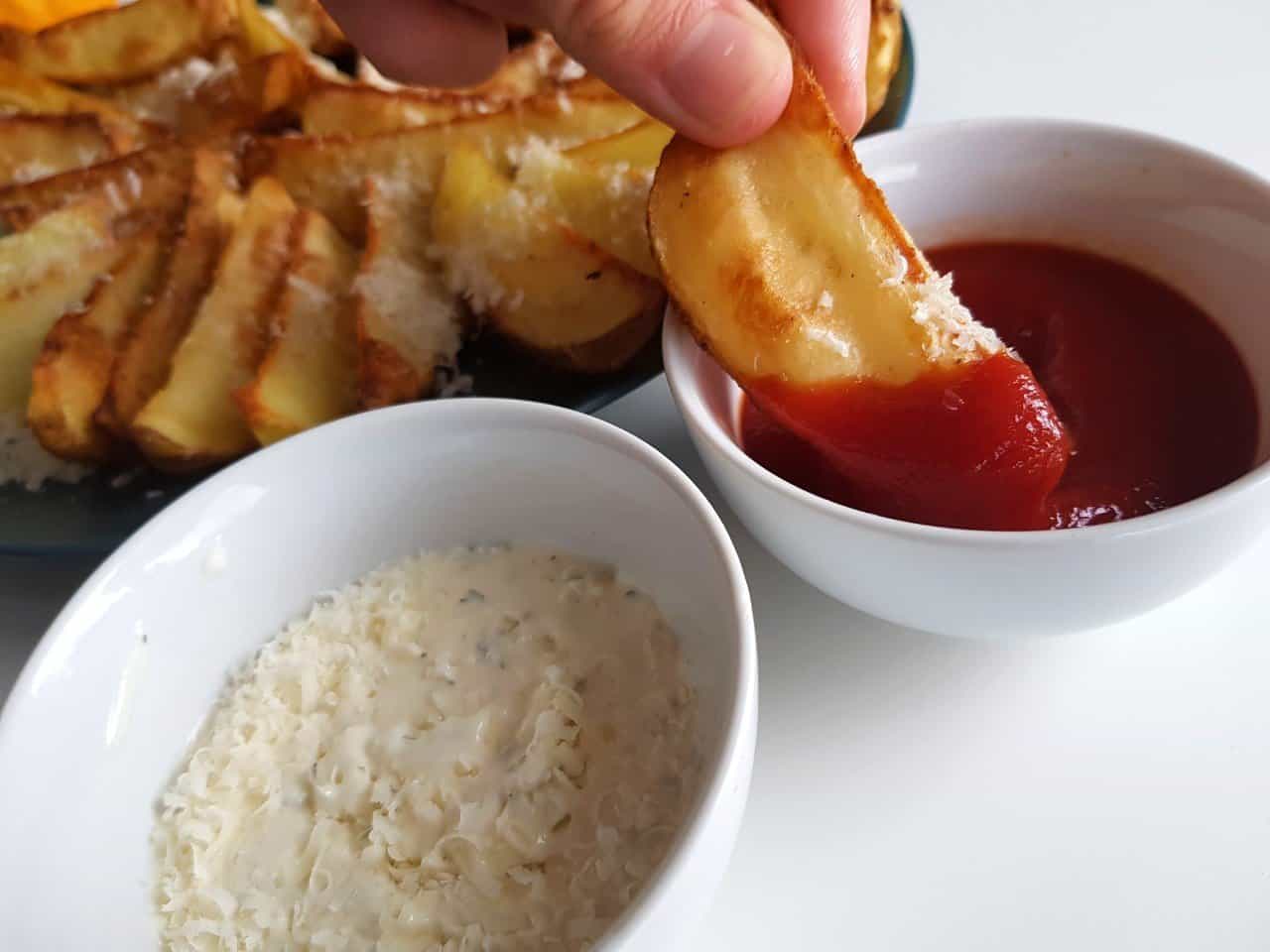 Crispy potato wedges dipped into ketchup.