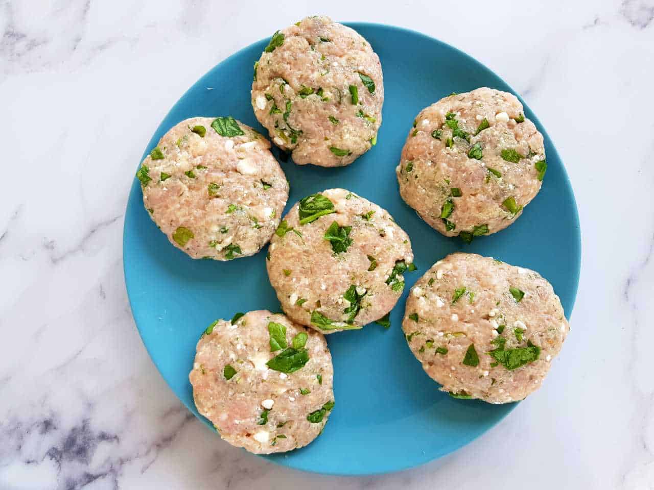 Greek turkey burger patties on a blue plate on a marble table.