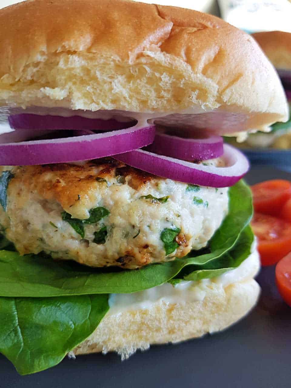 Greek turkey burger with red onion and lettuce on a blue plate with tomatoes on the side.