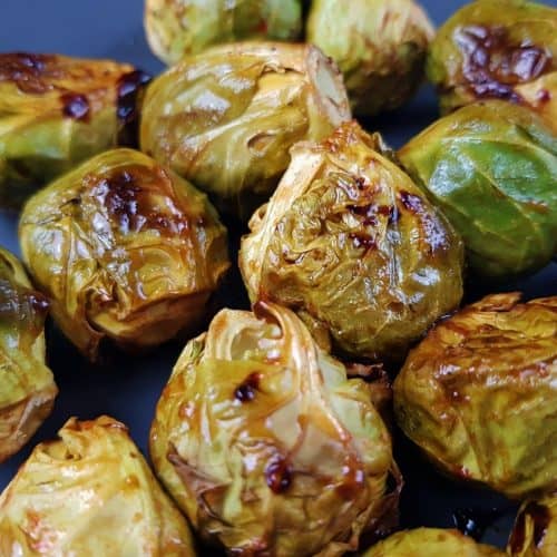 Roasted brussel sprouts with honey and sriracha on a dark plate.