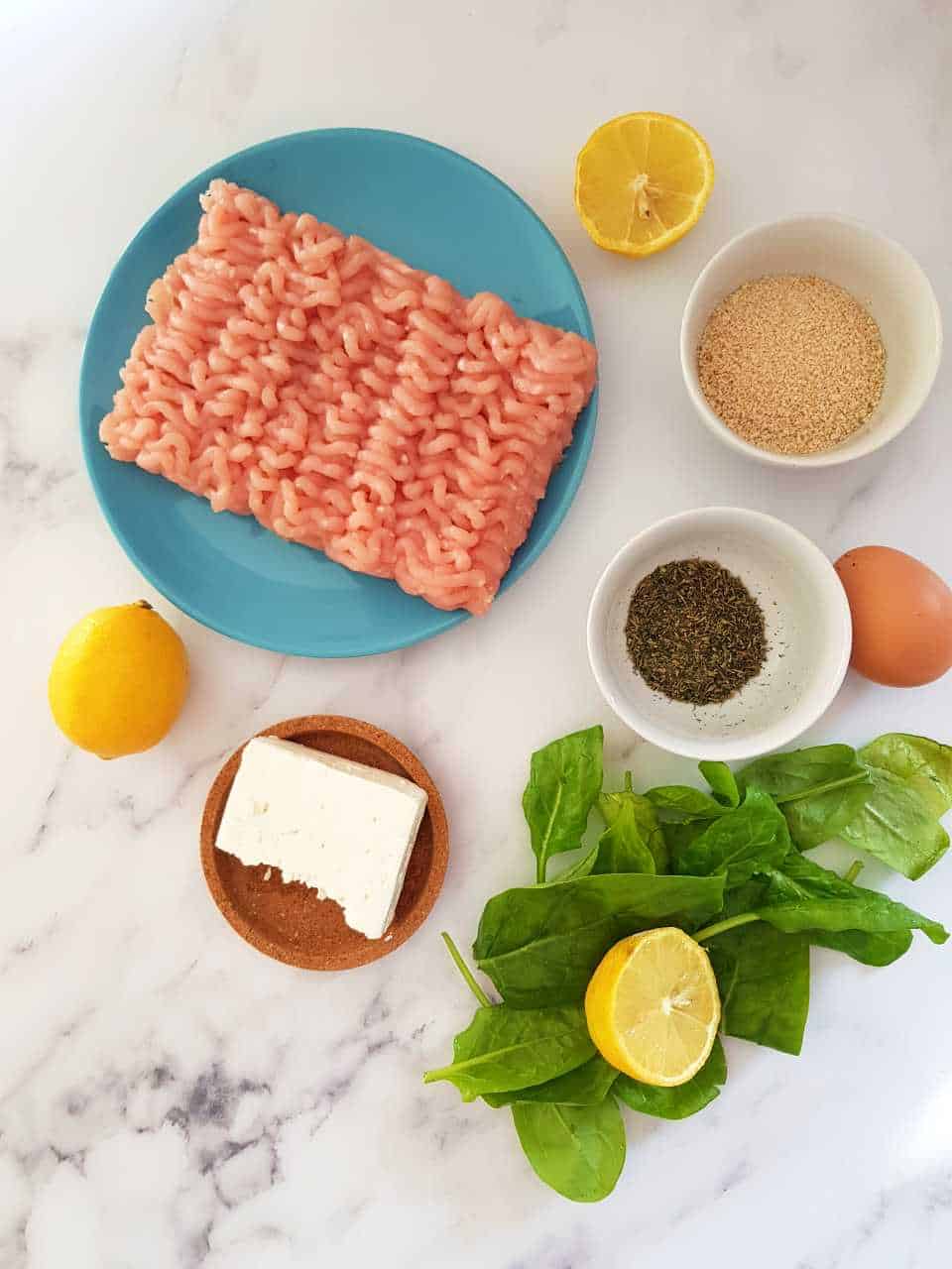 Ingredients for Greek turkey burger placed in bowls on a marble table.