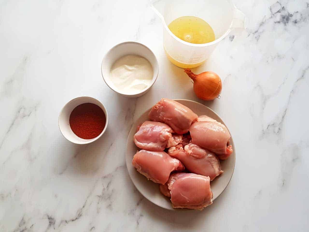 Chicken, paprika, sour cream, onion and chicken stock placed in bowls on a marble table.