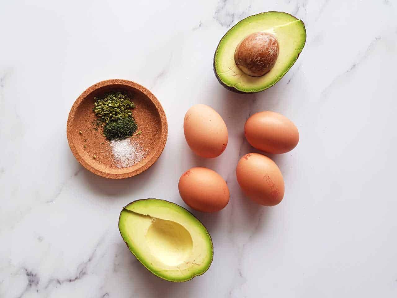 Eggs, avocado and herbs sitting on a marble table.