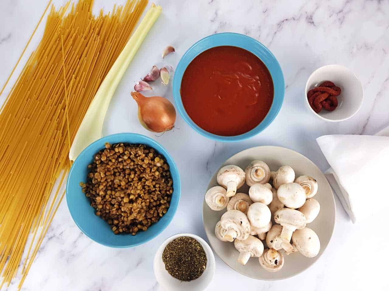 Ingredients for mushroom and lentil bolognese laid out on a marble table.