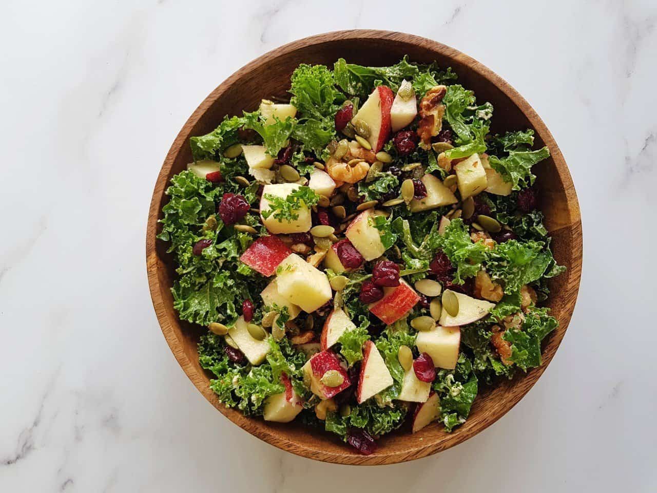 Kale salad with apples in a wooden bowl on a marble table.