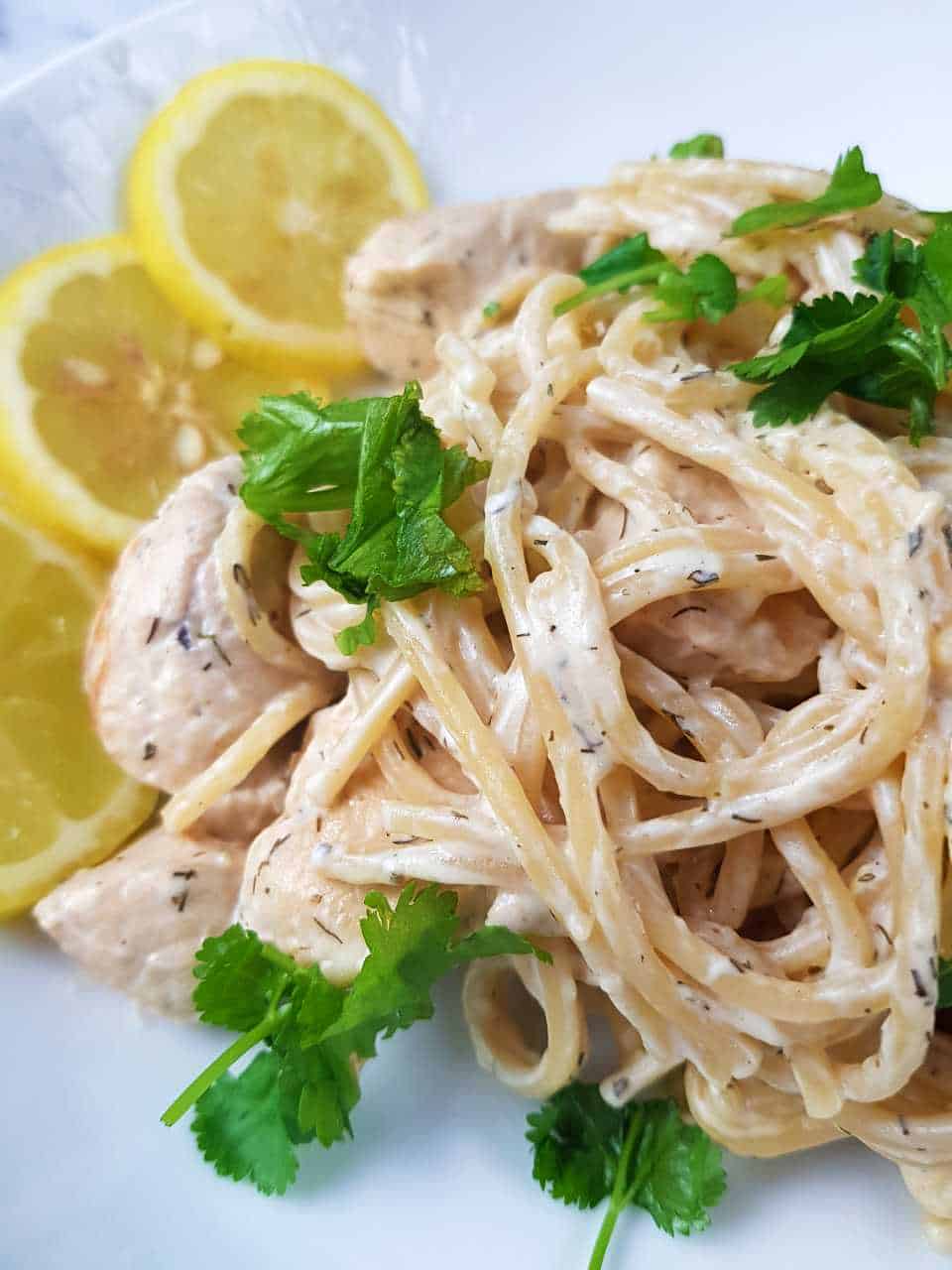 Plate of lemon chicken pasta topped with coriander, with lemon slices on the side.