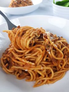 Lentil and mushroom bolognese on a white plate, with a fork lifting it up.