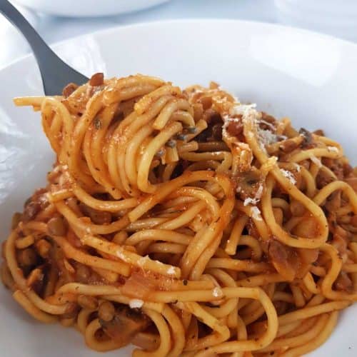Lentil and mushroom bolognese on a white plate, with a fork lifting it up.