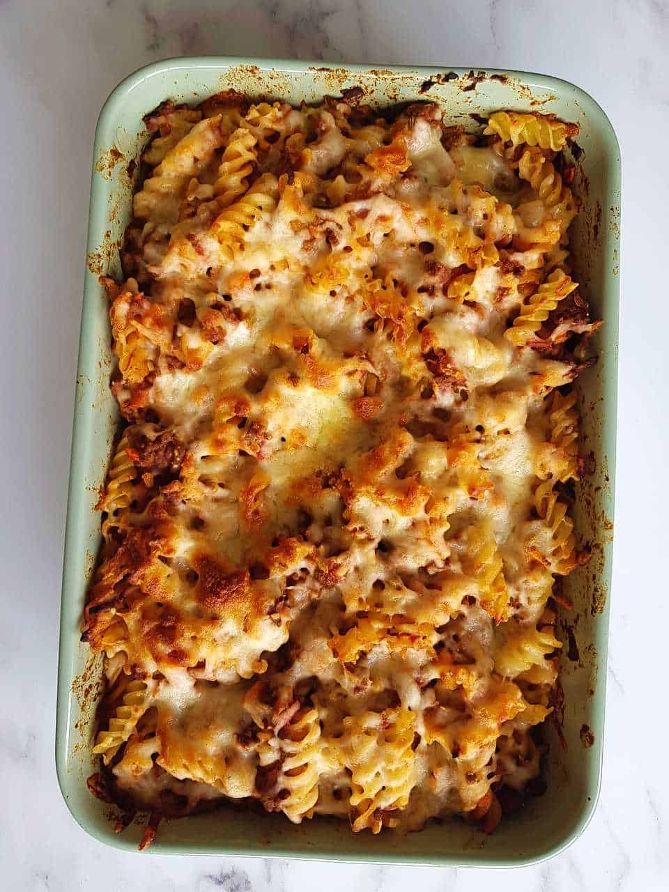 Minced beef pasta bake in a casserole dish on a marble table.