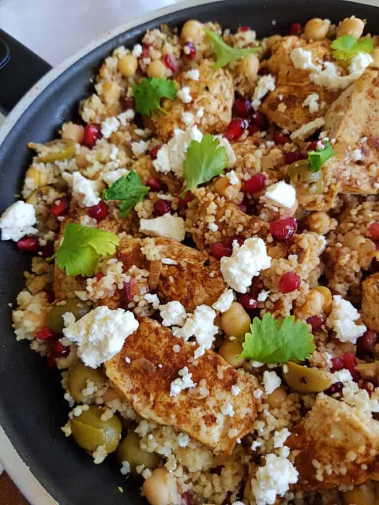 Moroccan chicken and couscous in a black skillet, with coriander and feta cheese on top.