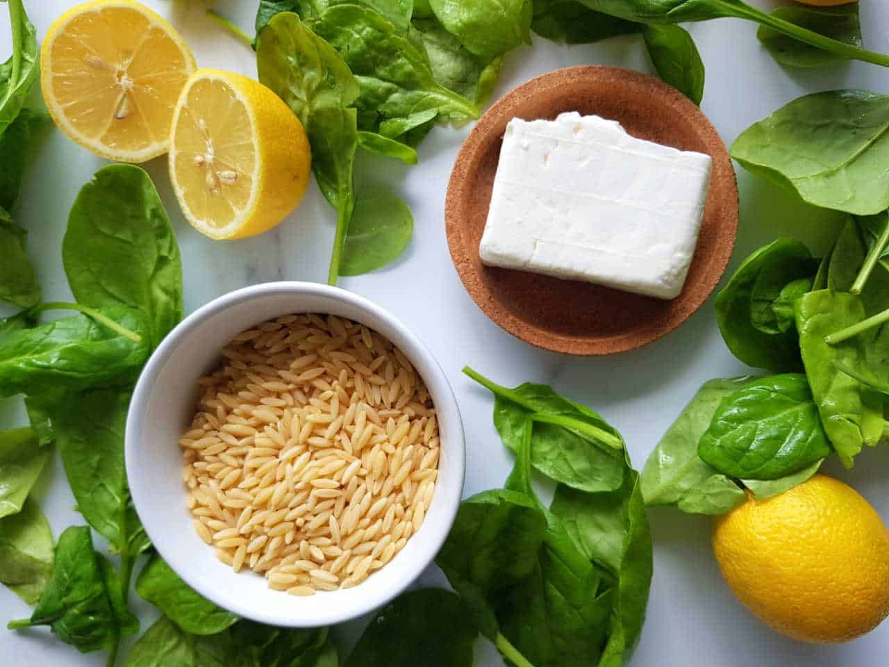 Spinach, feta, orzo and lemon on a marble table.