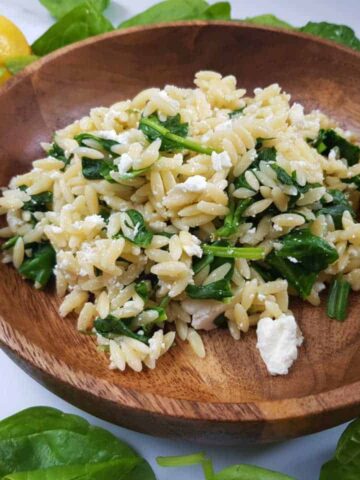 Orzo salad in a wooden bowl with lemon slices on the side.