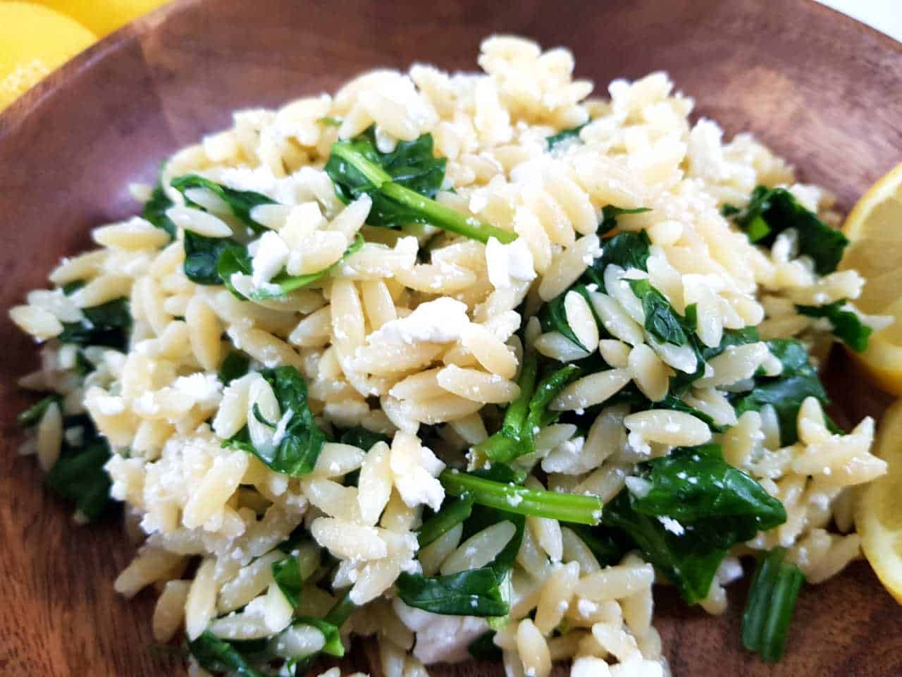 Orzo salad with spinach in a wooden bowl.