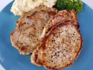 Pork loin steaks on a blue plate with mashed potatoes and broccoli.