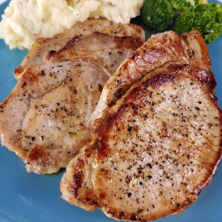 Pork loin steaks on a blue plate with mashed potatoes and broccoli.