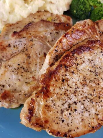 Pork loin steaks on a blue plate with mashed potatoes and broccoli.