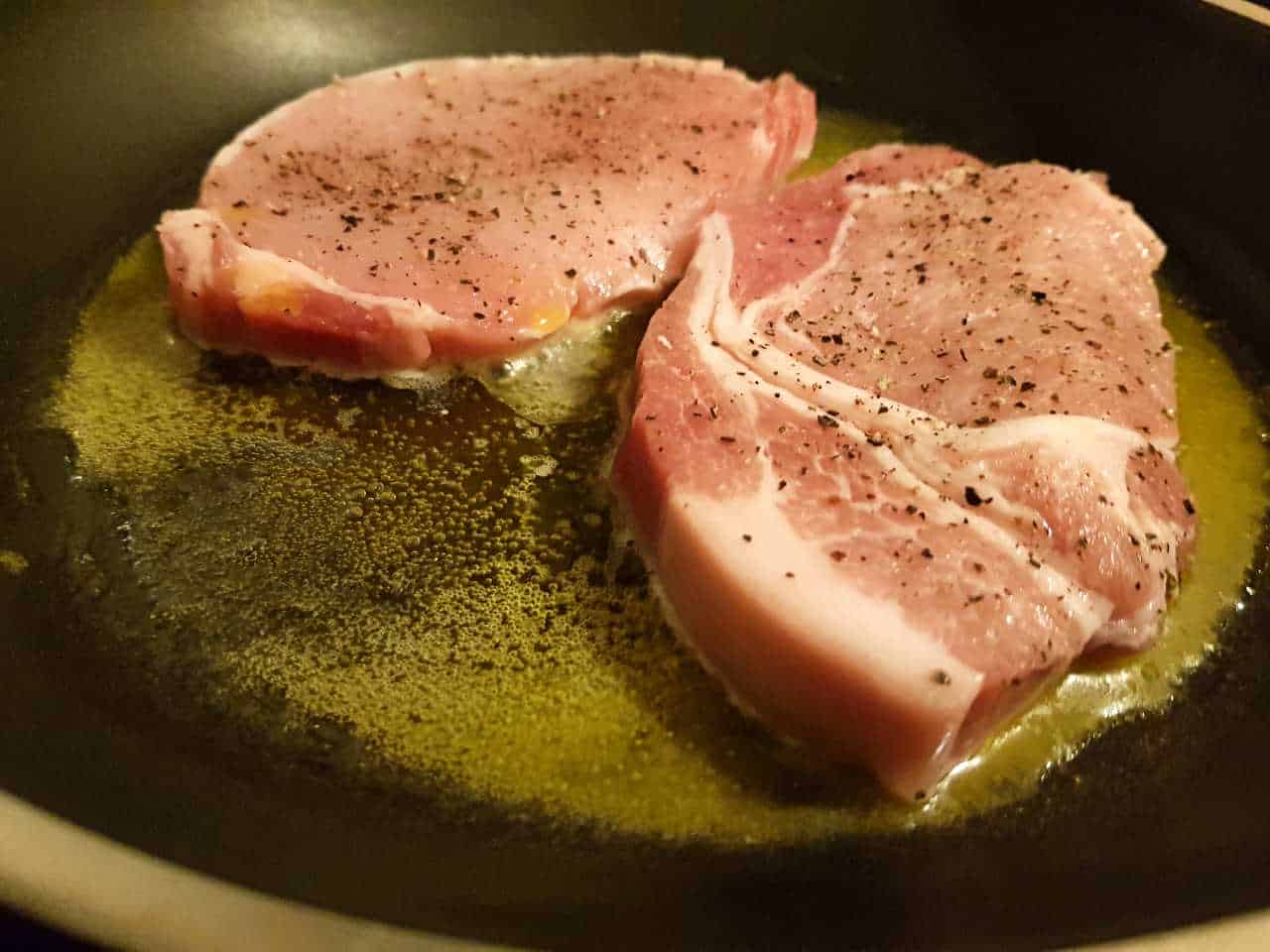 Two pork loin steaks cooking in a black pan.