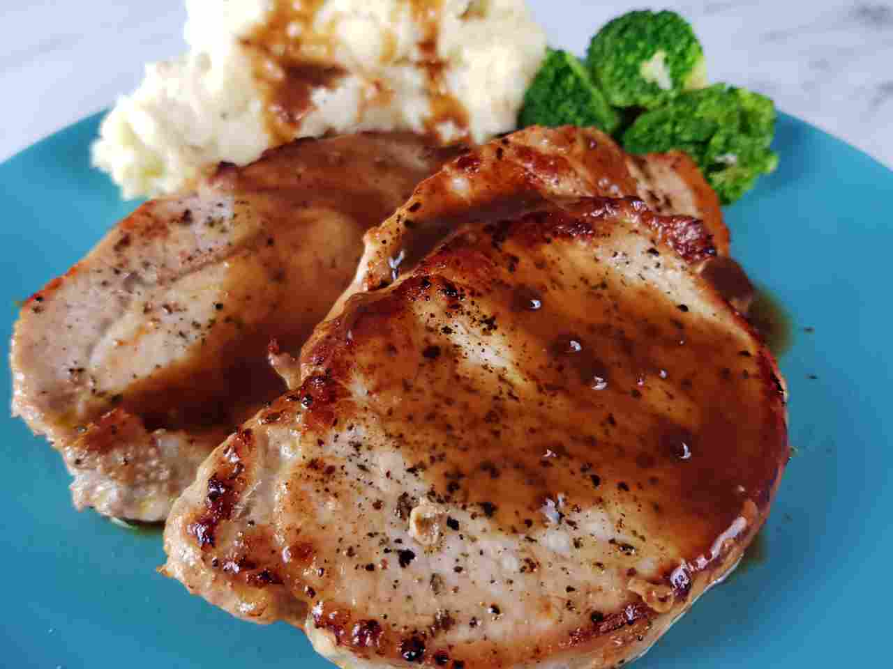 Pork loin steaks with gravy, mashed potatoes and broccoli on a blue plate.