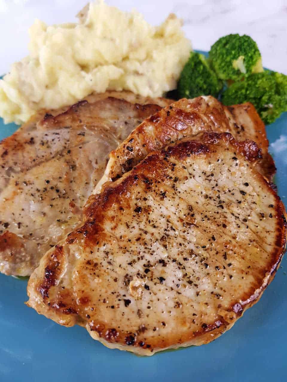 Pork steaks on a blue plate with mashed potatoes and broccoli.