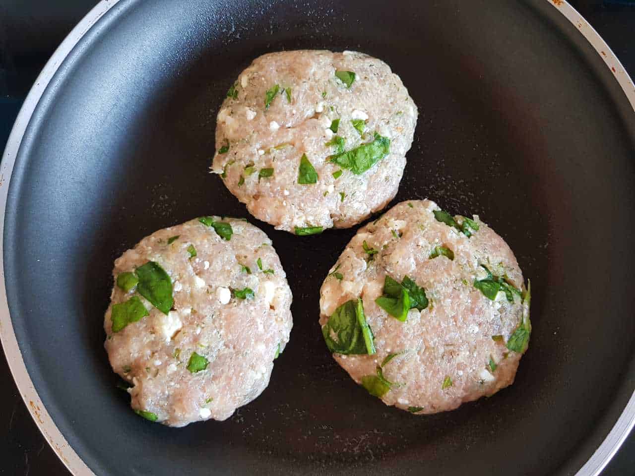 Raw Greek turkey burgers in a frying pan.