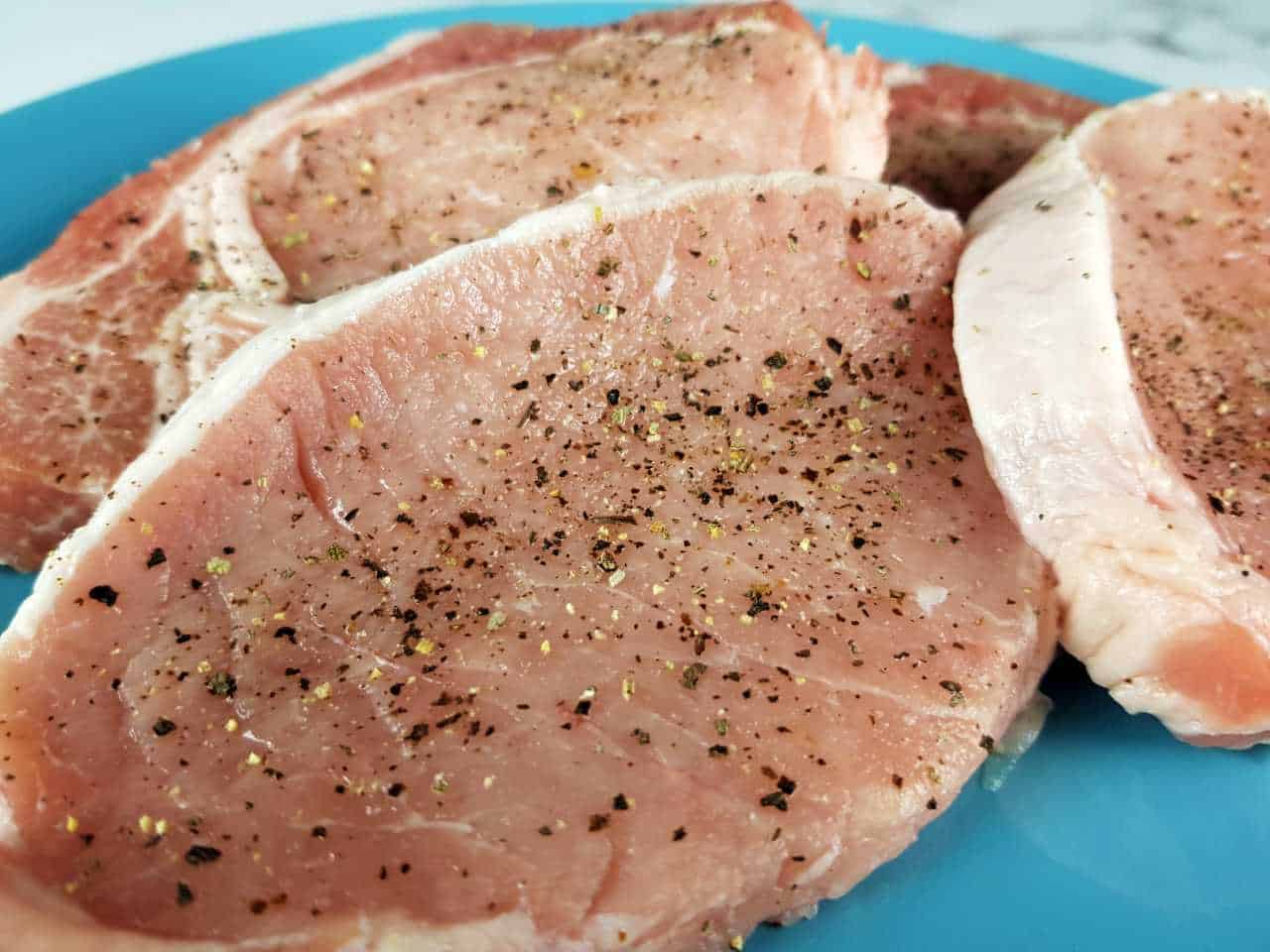 Raw pork loin steaks on a blue plate.