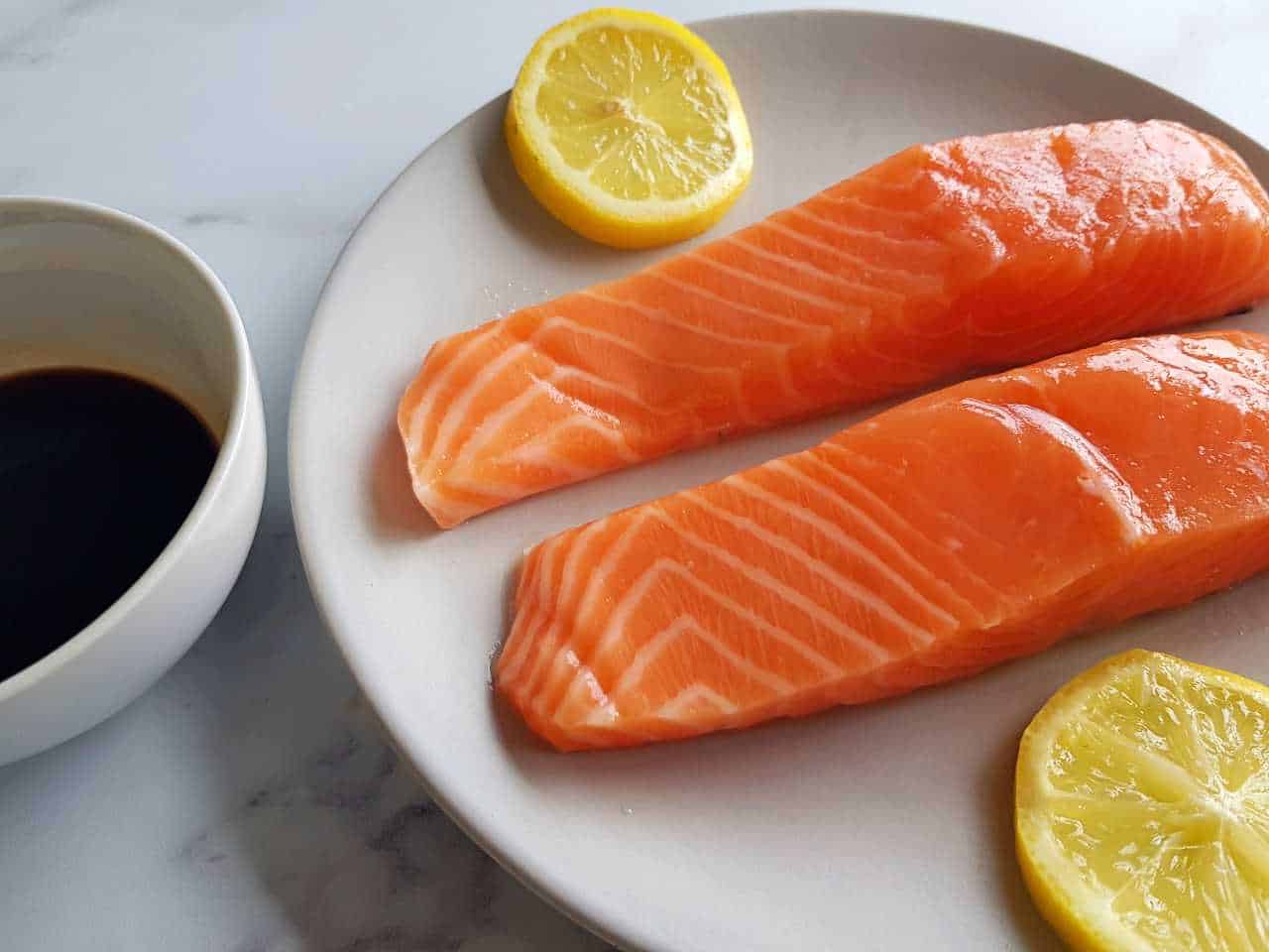 Raw salmon fillet on a plate with lemon slices, and a bowl of balsamic maple glaze.