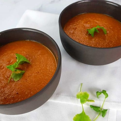 Spicy red lentil soup in black bowls on a marble table with coriander, a white napkin and lentils in front.