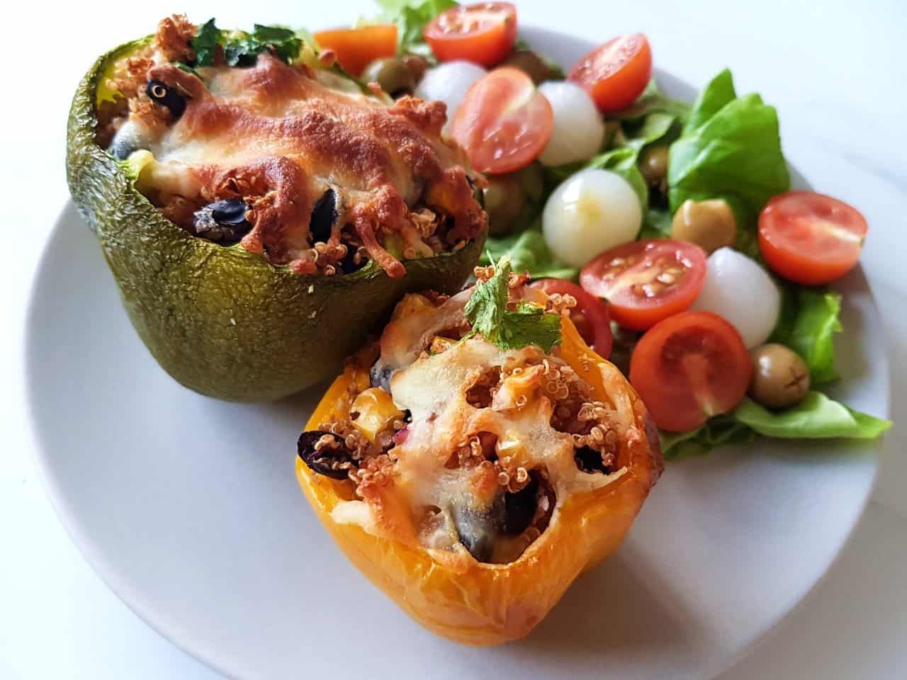 Stuffed green and yellow pepper on a grey plate with a salad in the background.