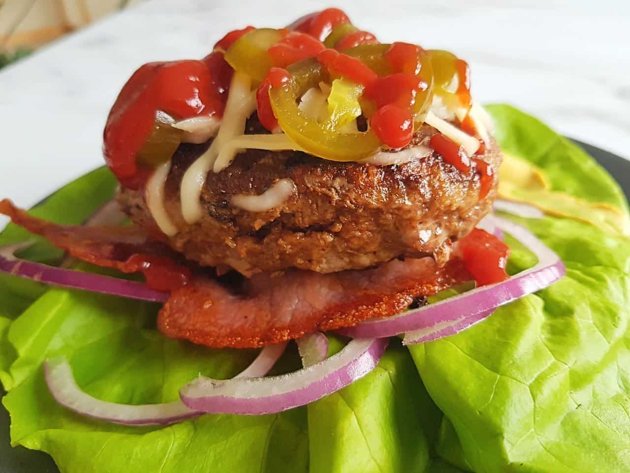 Beef burger patty on salad leaves with toppings.