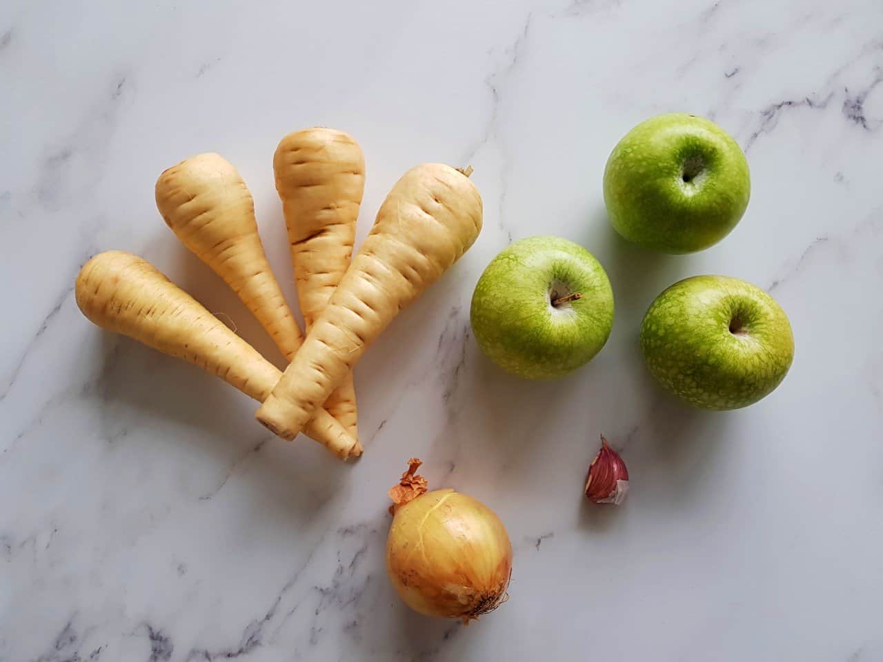 Raw parsnips, green apples, onion and garlic laid on a table.