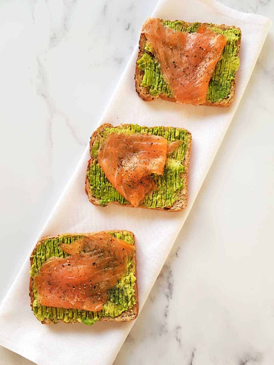 Avocado toast with smoked salmon on a white napkin on a marble table.