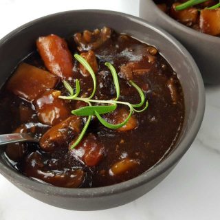 Beef and ale stew in gray bowls with spoons on a marble table.