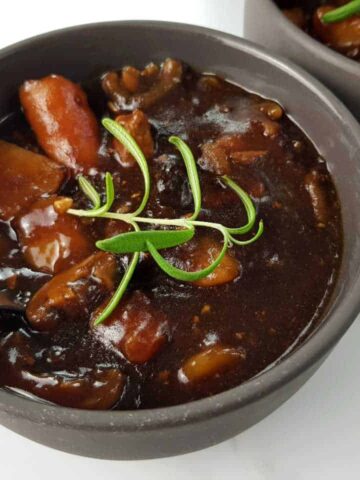 Beef and ale stew in gray bowls with spoons on a marble table.